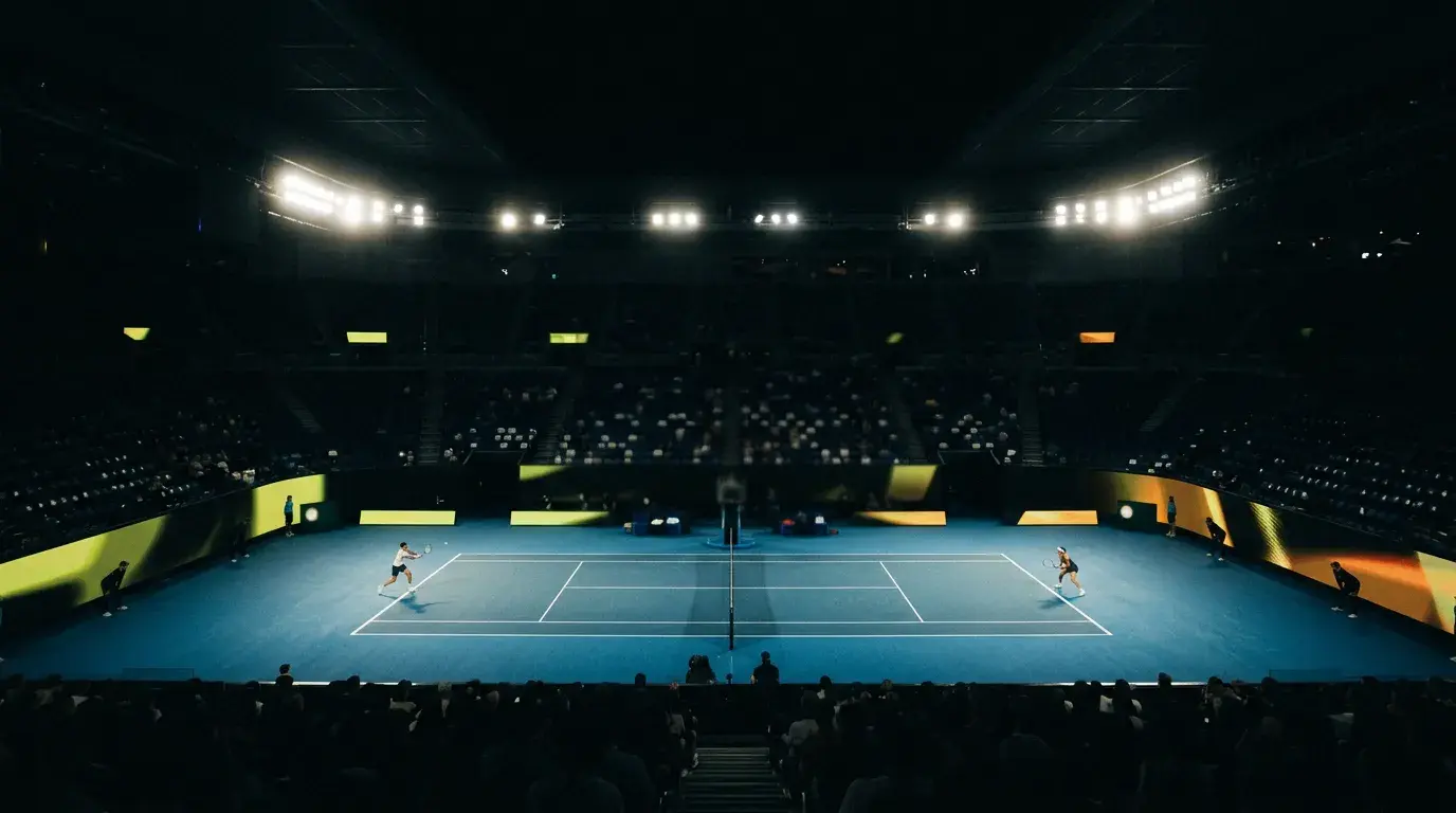 Pista de tenis profesional iluminada durante un partido nocturno visto desde la tribuna, atmósfera de competición en vivo